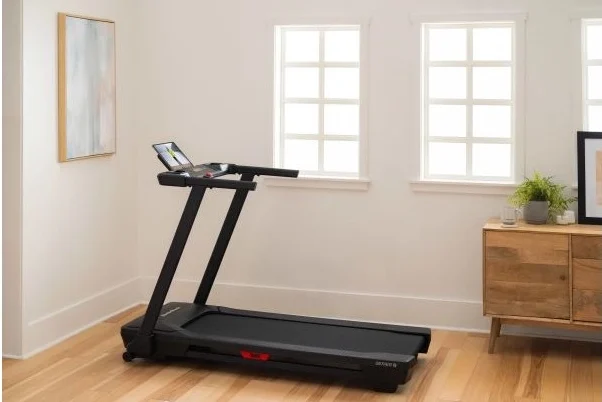 NordicTrack T Series 5 folding treadmill set up in a minimalist home gym with natural wood sideboard and bright windows