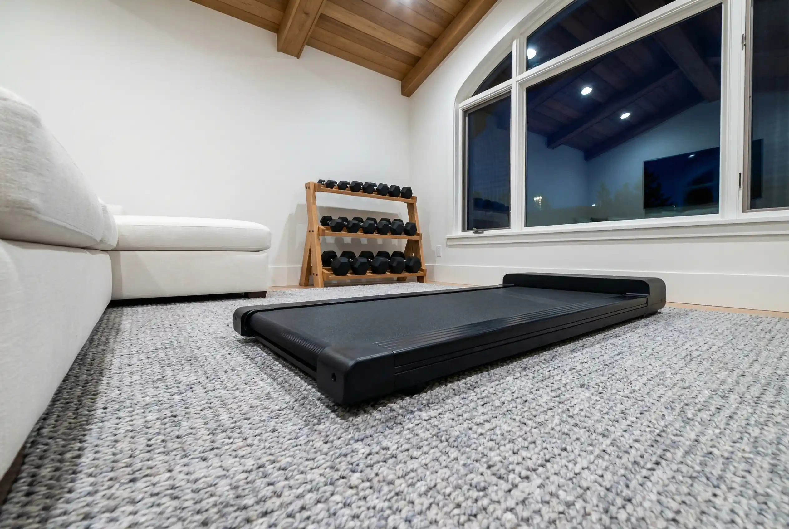 TRAILVIBER Walking Pad flat treadmill on carpet in a home setting with white furniture and dumbbell rack visible