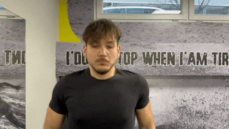 A close-up GIF of a man in a gym performing deep breathing exercises, showing controlled inhalation and exhalation.