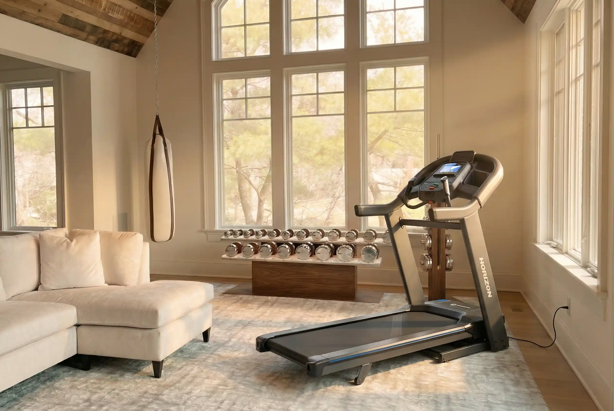 Horizon Fitness 7.4 AT treadmill in bright home gym with arched windows, exposed beam ceiling, and chrome dumbbell set on windowsill