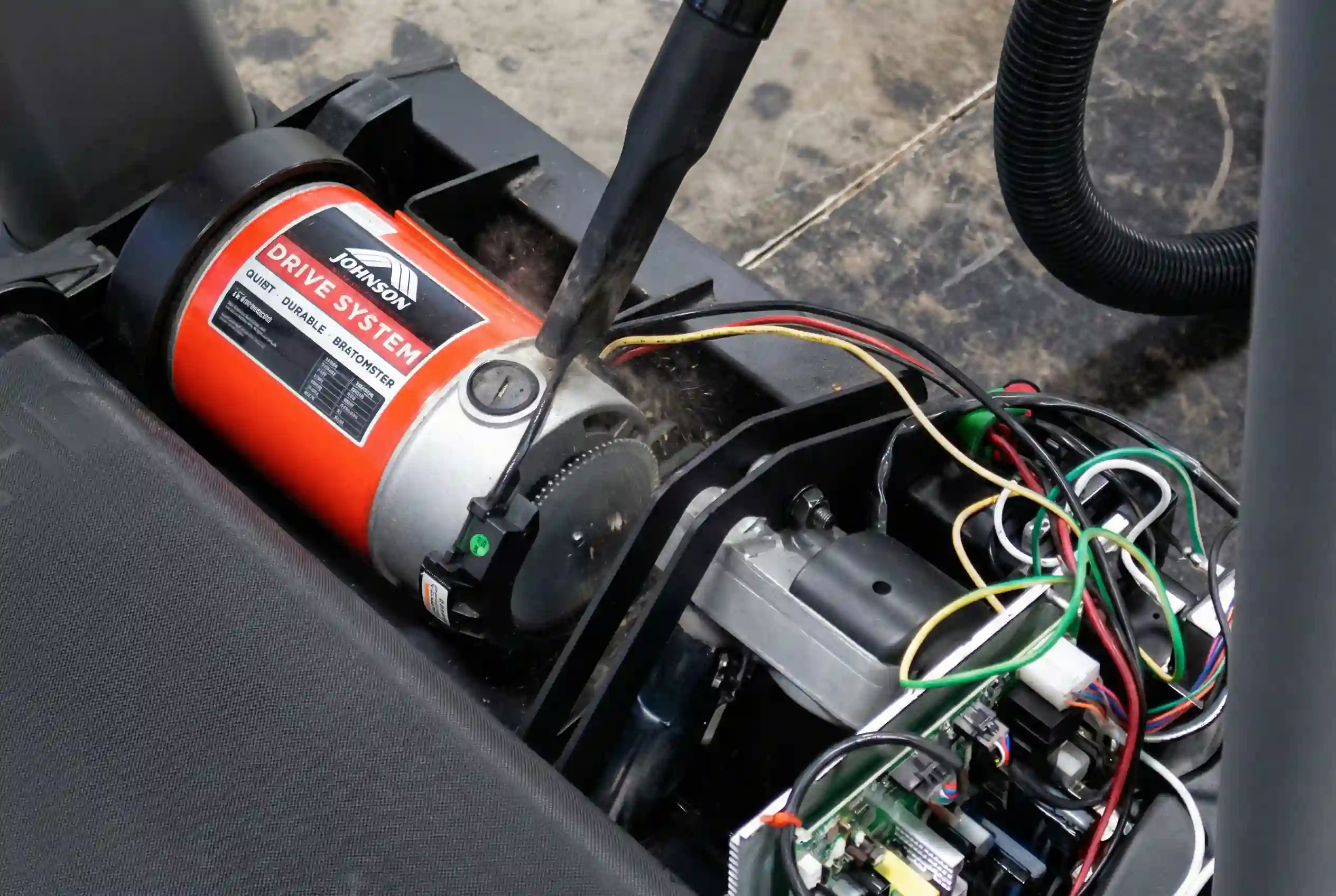 Vacuum hose cleaning dust and debris from Horizon T202 treadmill motor compartment with orange drive system motor and exposed electrical wiring visible during maintenance