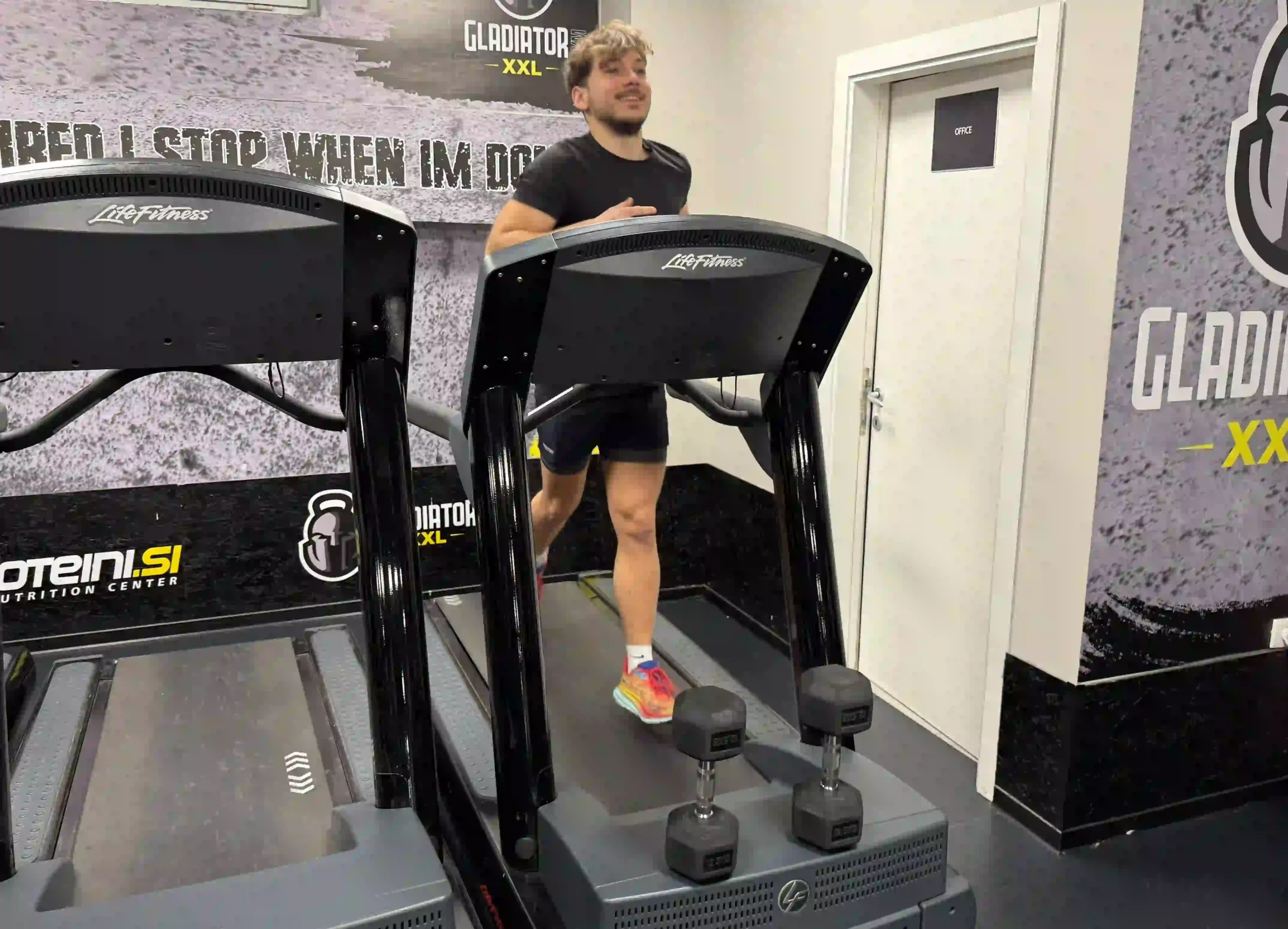 Milutin smiling while running on commercial treadmill in black shirt and shorts at gym facility