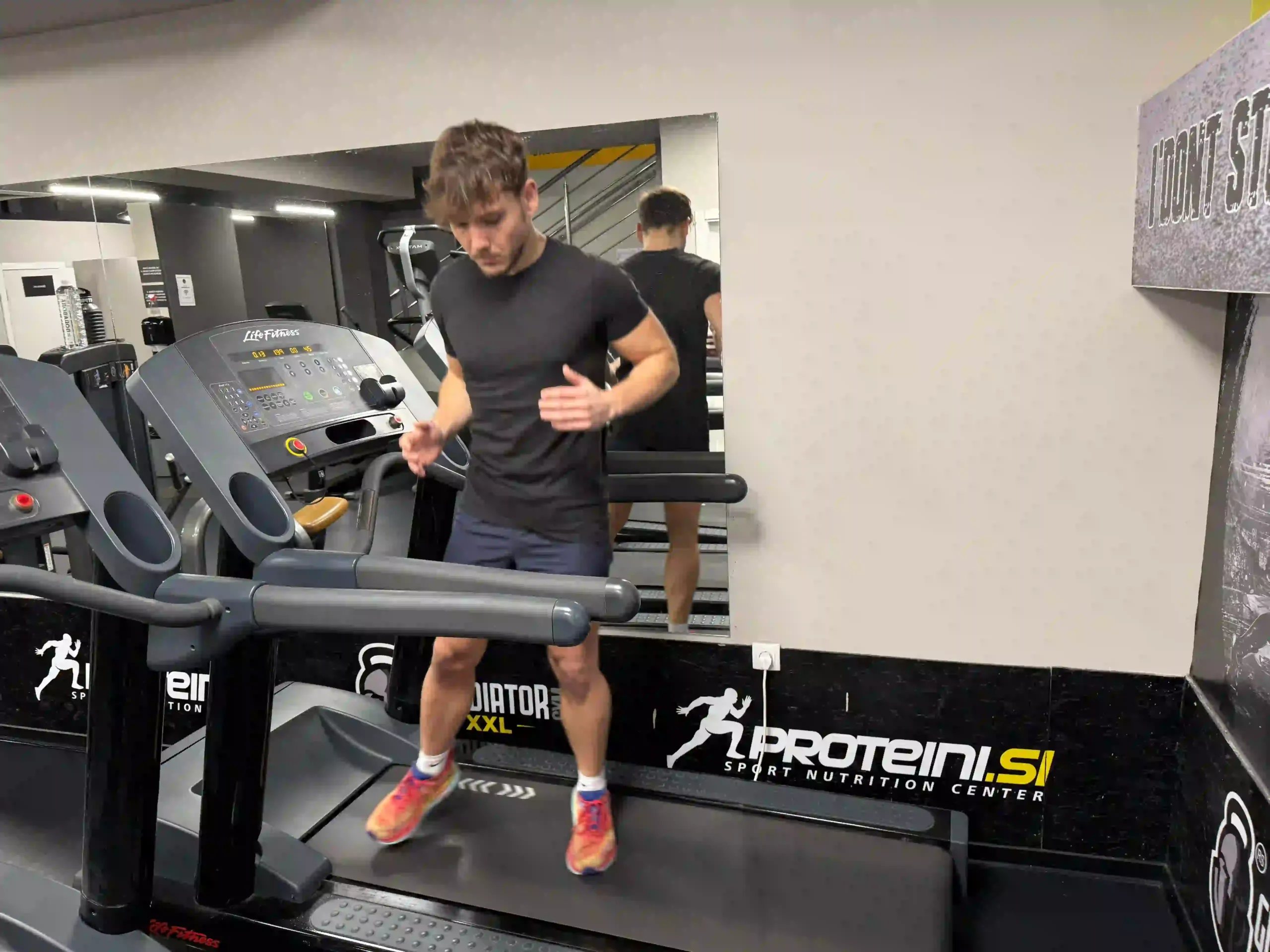 Milutin in athletic wear performing a sideways shuffling exercise on a moving treadmill in a gym.