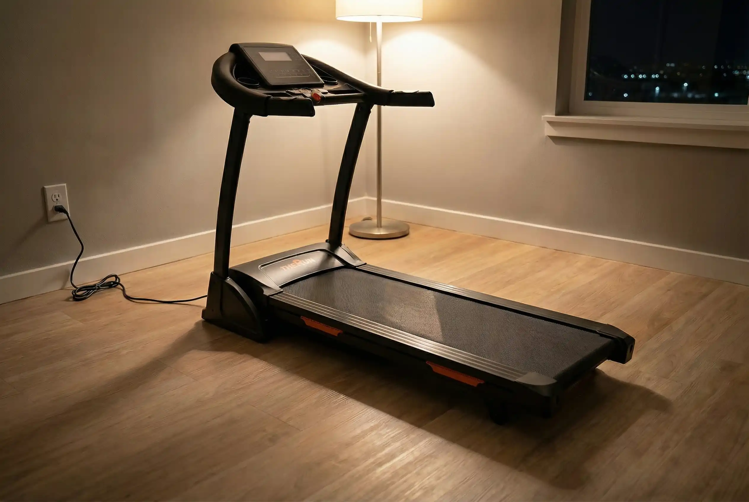 TheRun Folding Incline Treadmill with orange accent trim positioned in corner with modern floor lamp and hardwood flooring