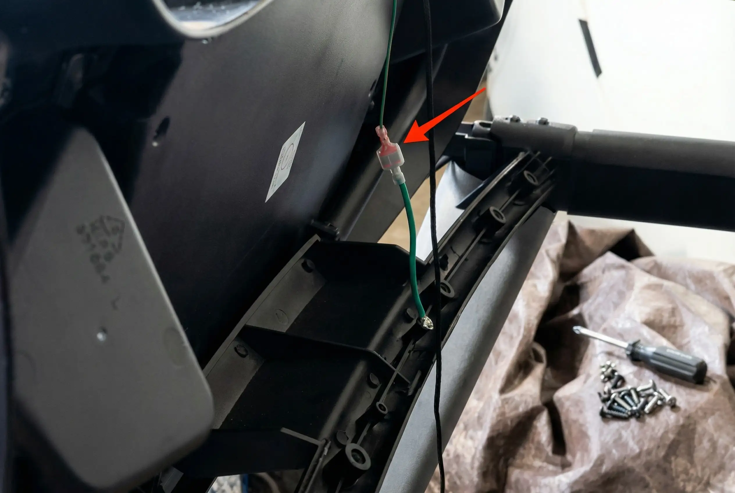 Treadmill console connector cable with red arrow indicating attachment point on black treadmill frame during disassembly, with green wiring visible and screws on cloth in background