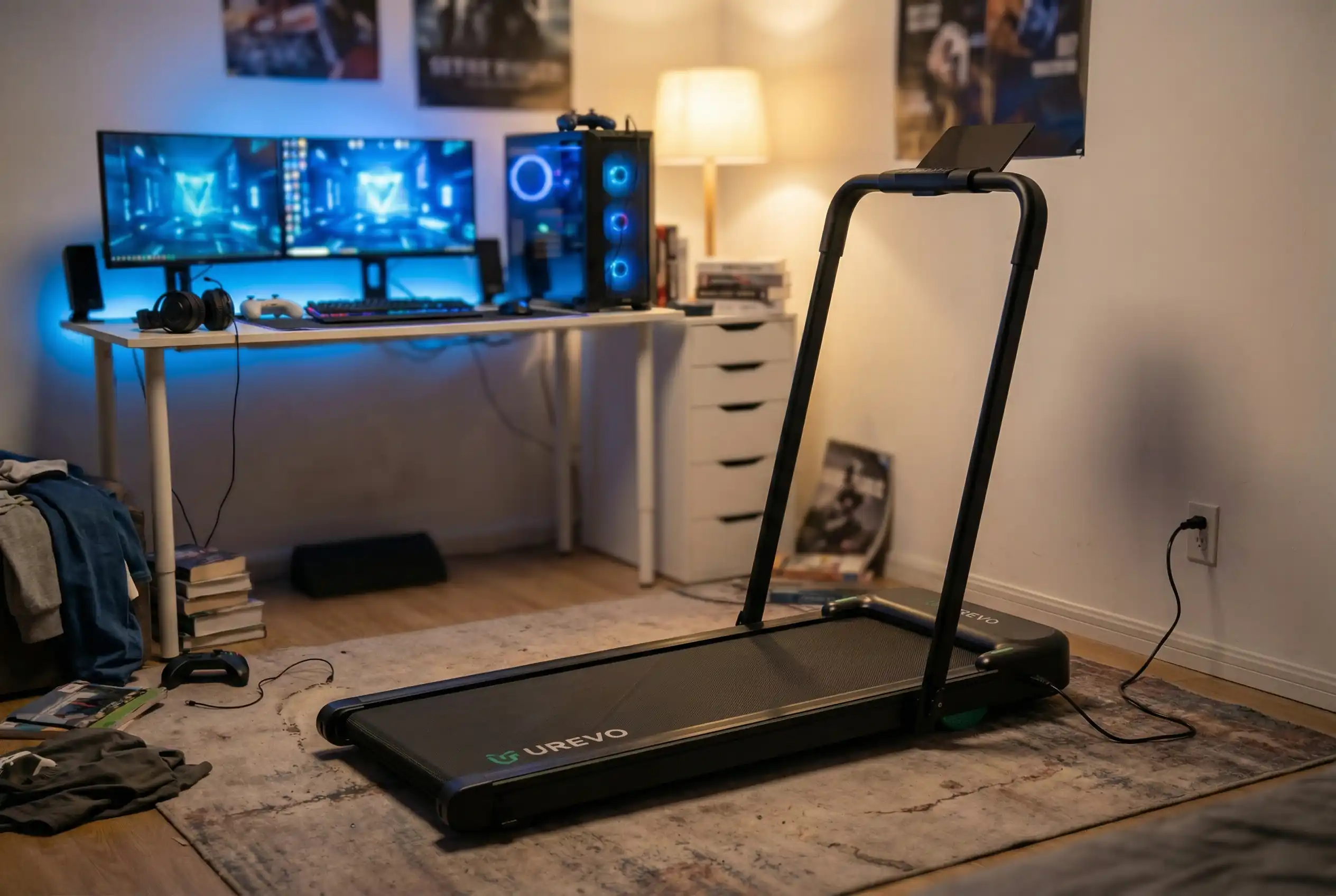 Urevo Stroll 2E treadmill with support handles in gaming room with dual monitor setup, RGB gaming PC, and LED desk lighting