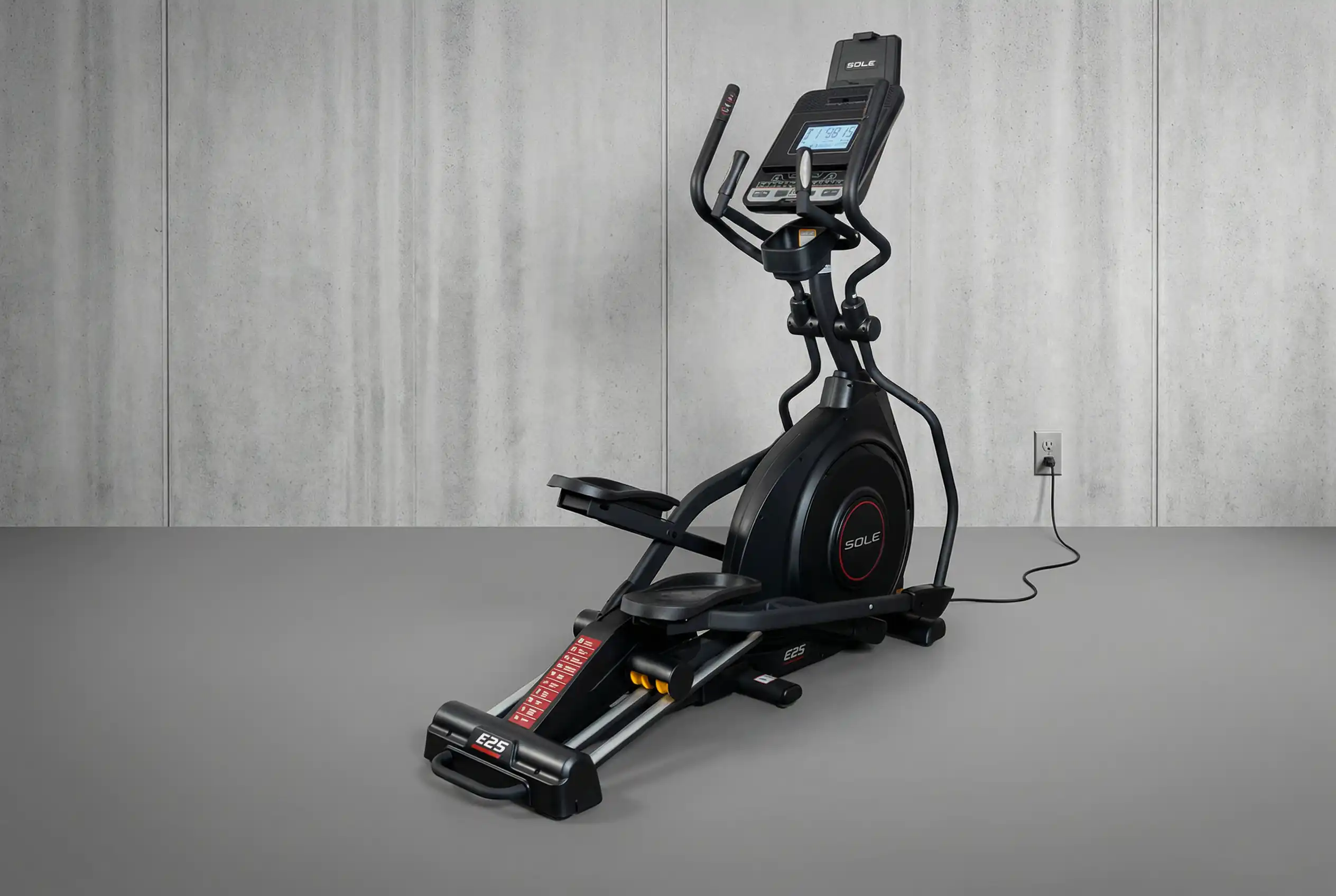 Sole-E25 Sole E25 elliptical machine with digital console, moving handlebars, and large flywheel positioned against industrial concrete wall backgroundSole E25 elliptical machine with digital console, moving handlebars, and large flywheel positioned against industrial concrete wall background