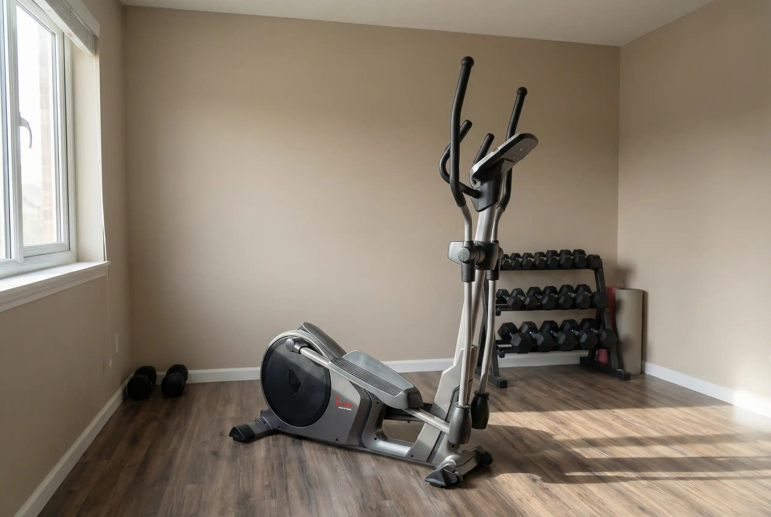 Sunny-Health-&-Fitness-CT Sunny Health & Fitness elliptical machine with moving handlebars and digital monitor in minimalist home gym with natural window lighting, laminate wood flooring, and dumbbell rack in corner