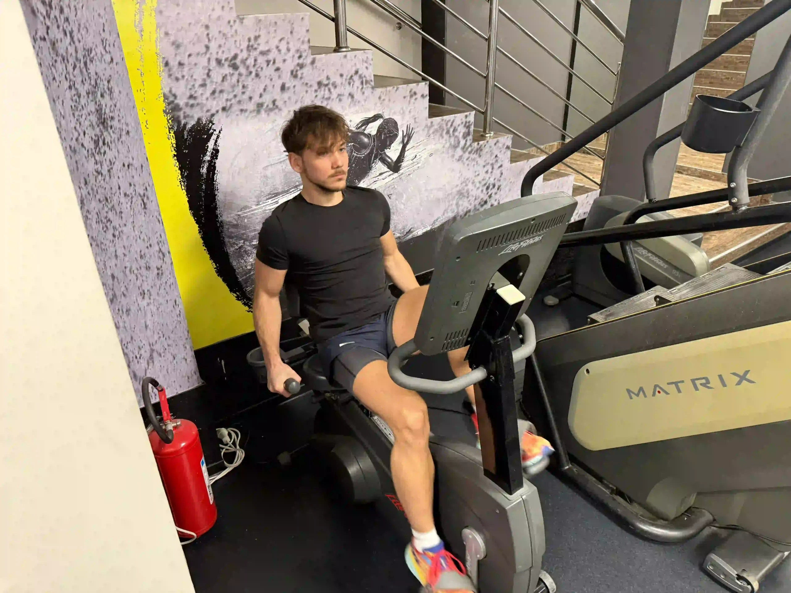Milutin cycling on an exercise bike in a commercial gym environment.
