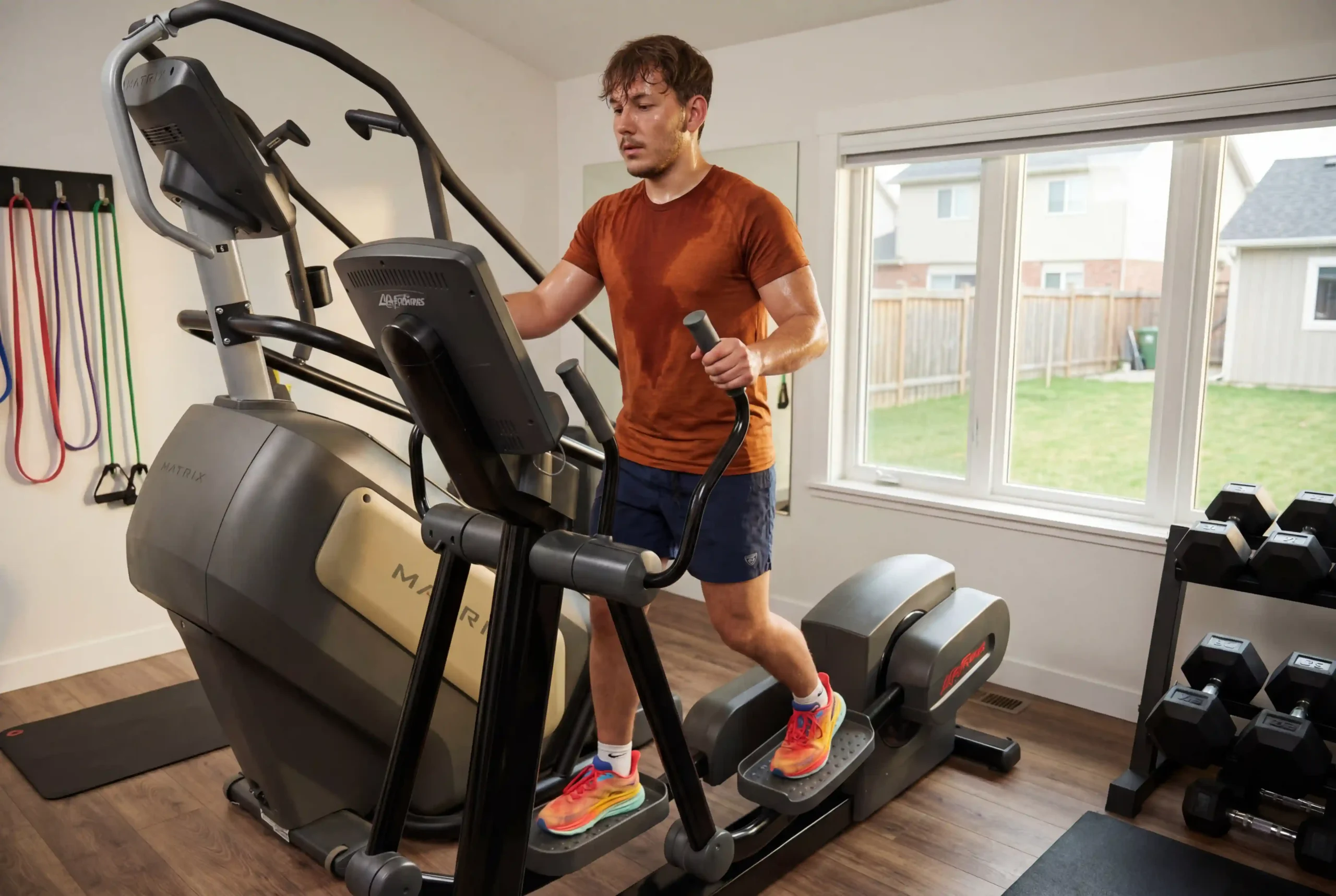 Milutin on an elliptical machine in a home gym environment, visibly sweaty from a HIIT elliptical workout.