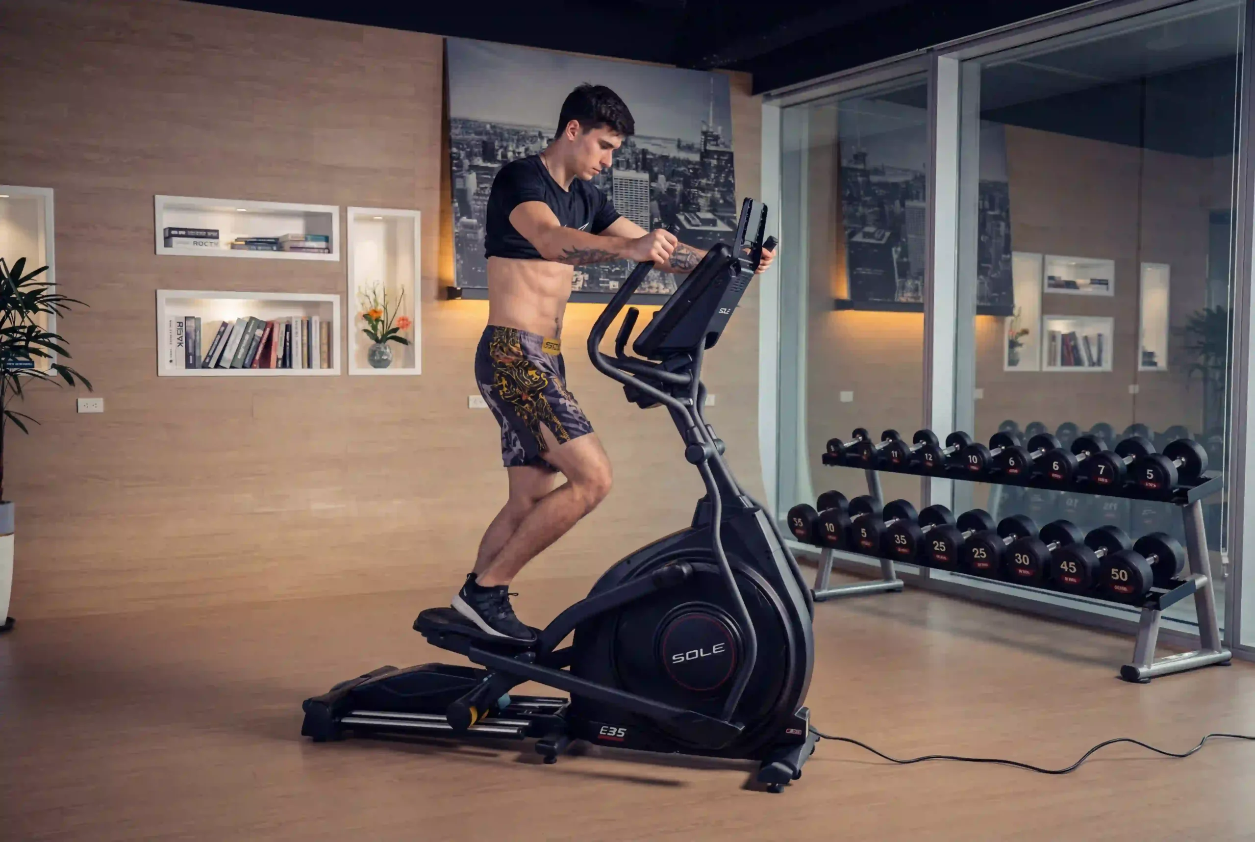 Vanja on Sole E25 in a home gym environment, t-shirt slightly pulled up so that the abs are showing and are contracted during the elliptical workout.