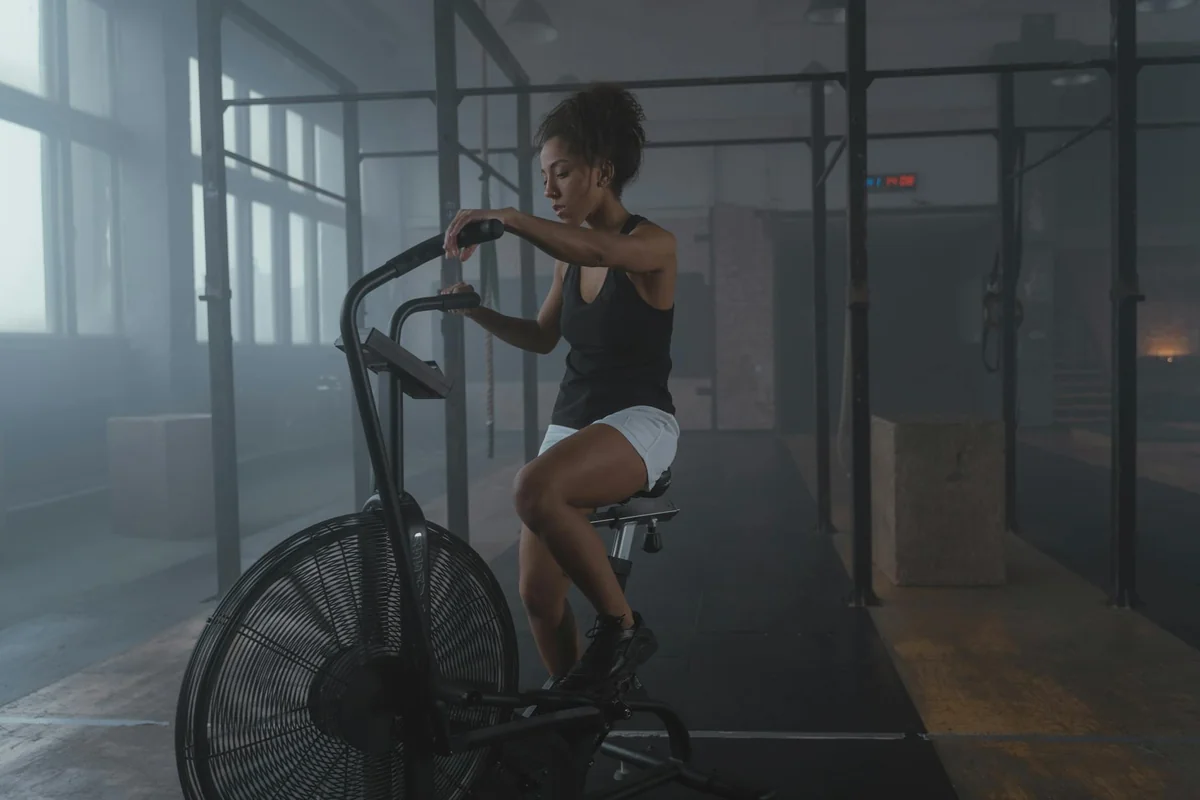 Woman cycling on a stationary air bike in an industrial gym with large windows