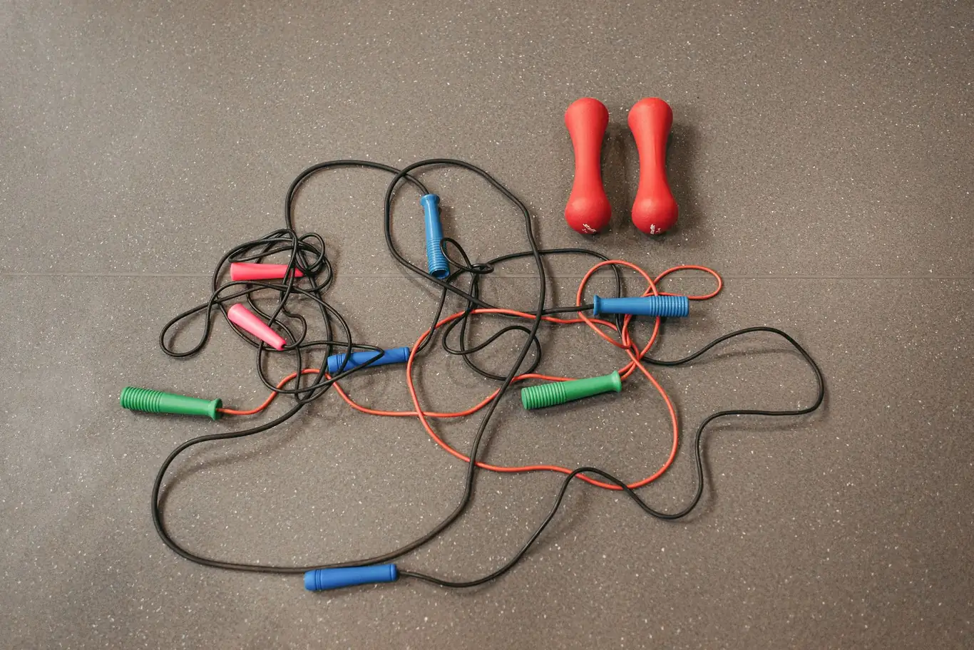 Jump ropes and red dumbbells scattered on gray rubber gym flooring
