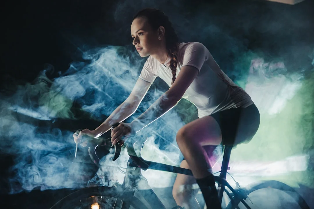 Woman cycling hard on a stationary bike surrounded by dramatic blue smoke in a dark studio