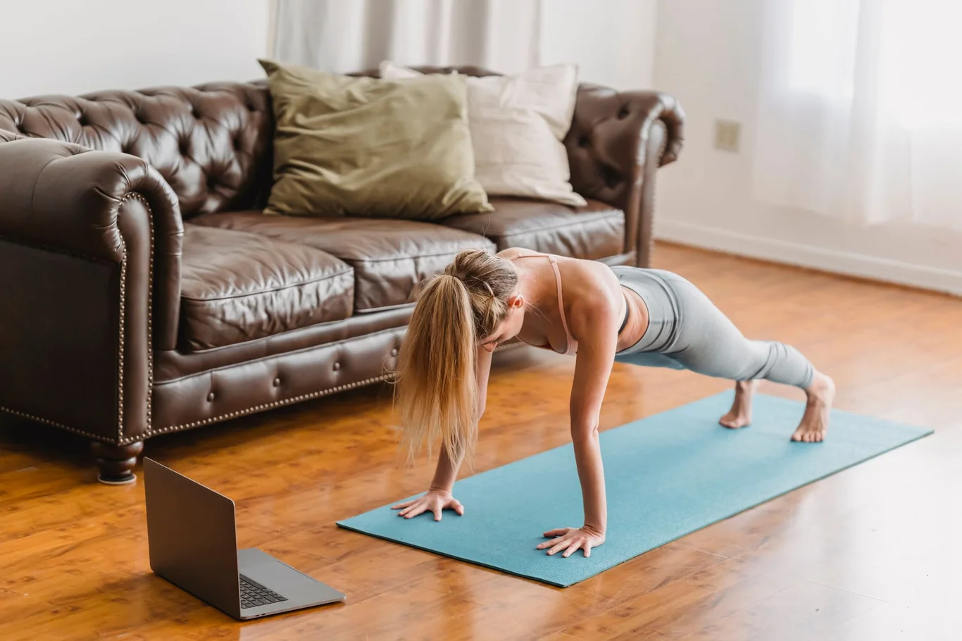 Woman doing a plank exercise on a yoga mat while following a fitness class on a laptop