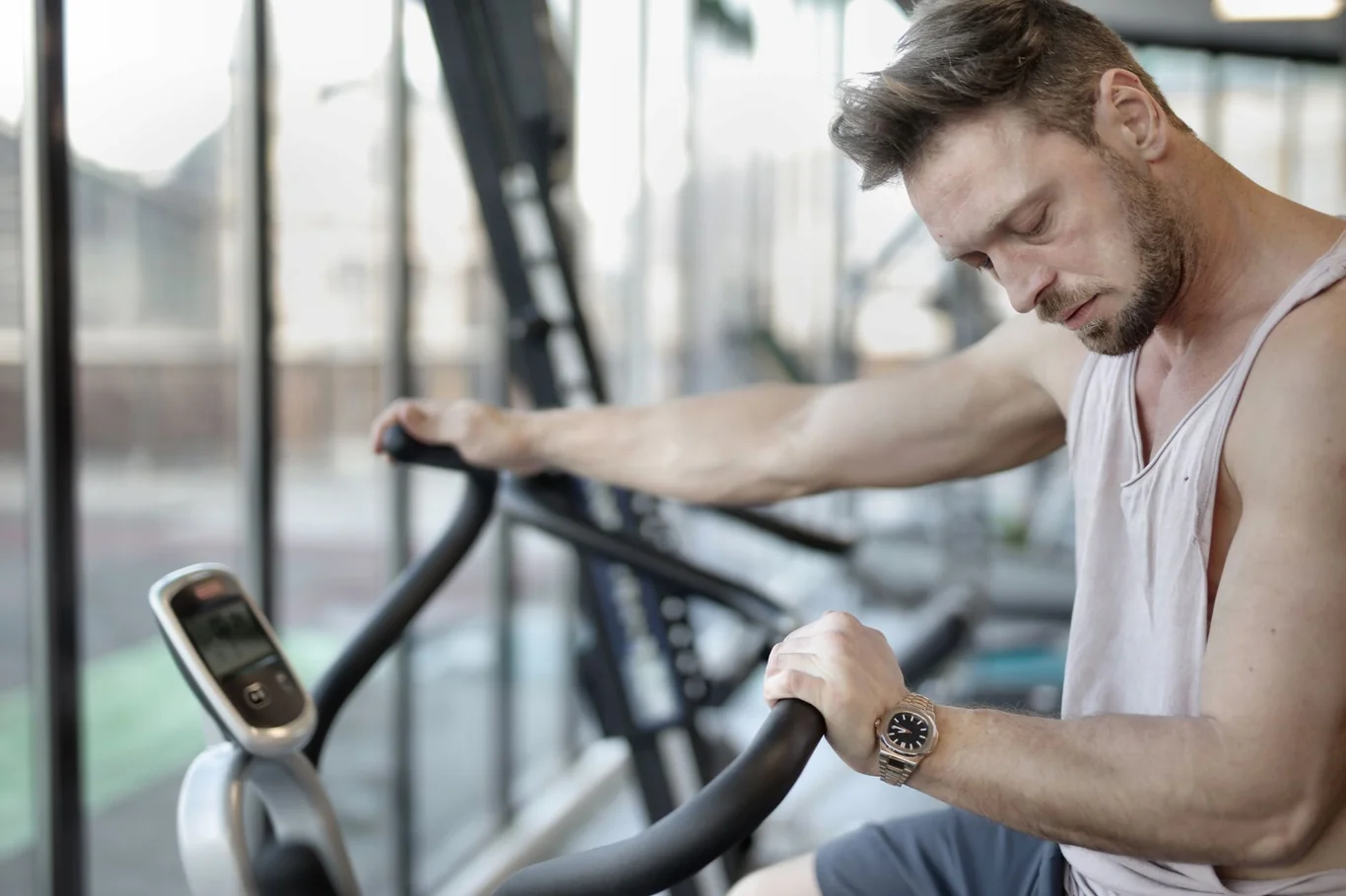 Man resting on an exercise bike at the gym, checking his watch