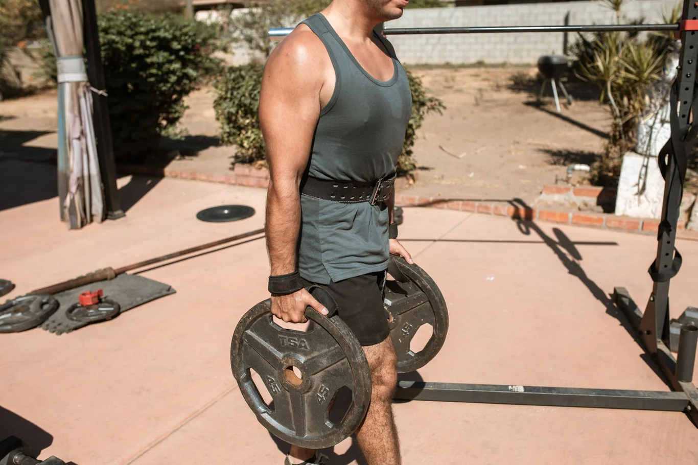 Man loading a barbell plate in an outdoor home gym with a squat rack in the background