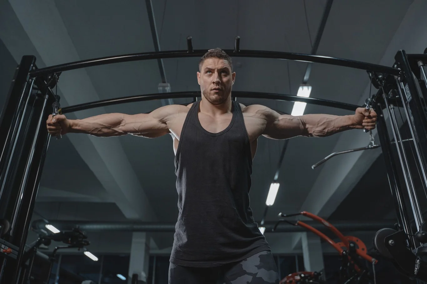Muscular man performing cable fly exercise on a cable machine in a modern gym
