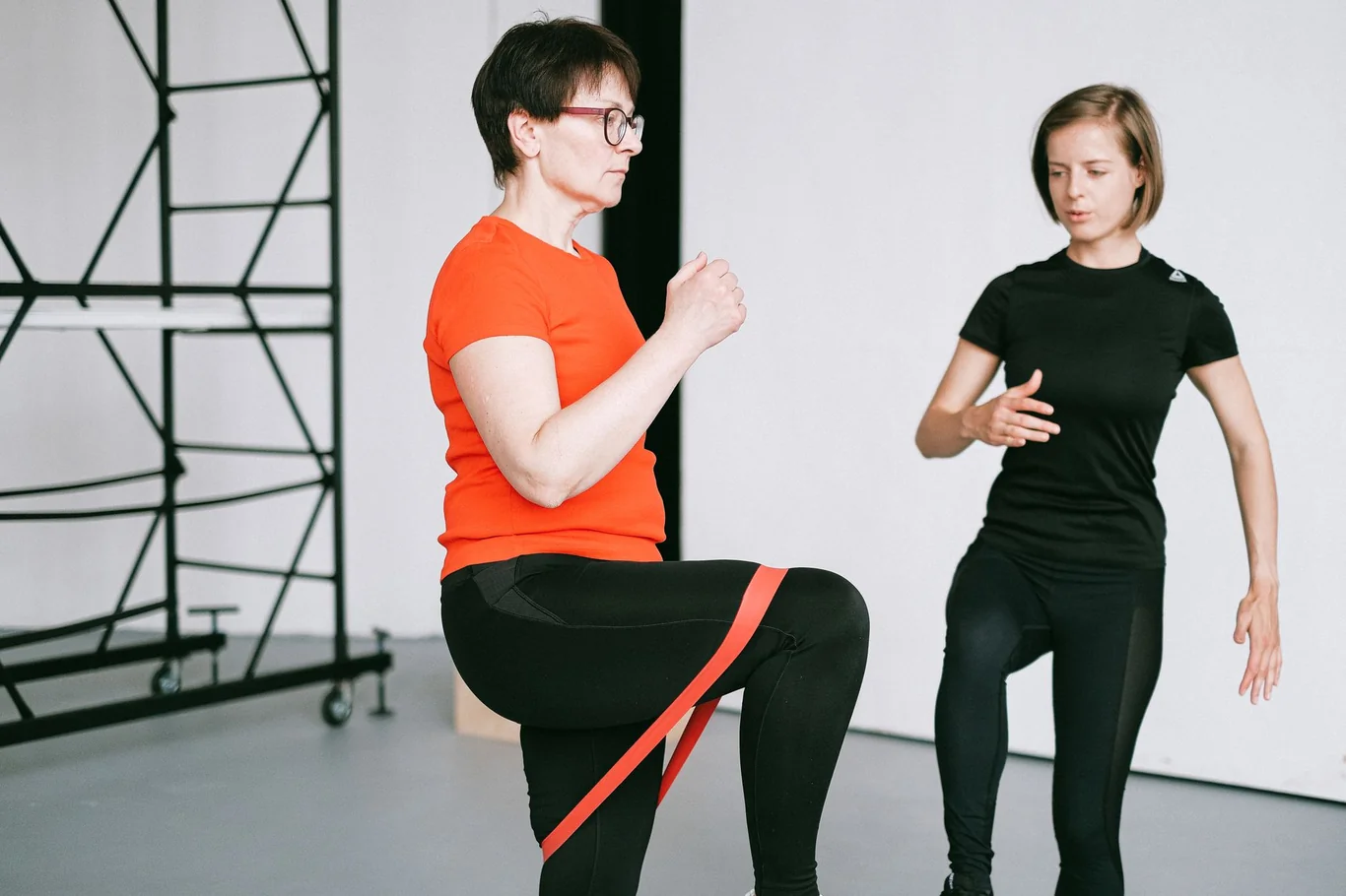 Trainer guiding a woman doing resistance band squats in a bright studio