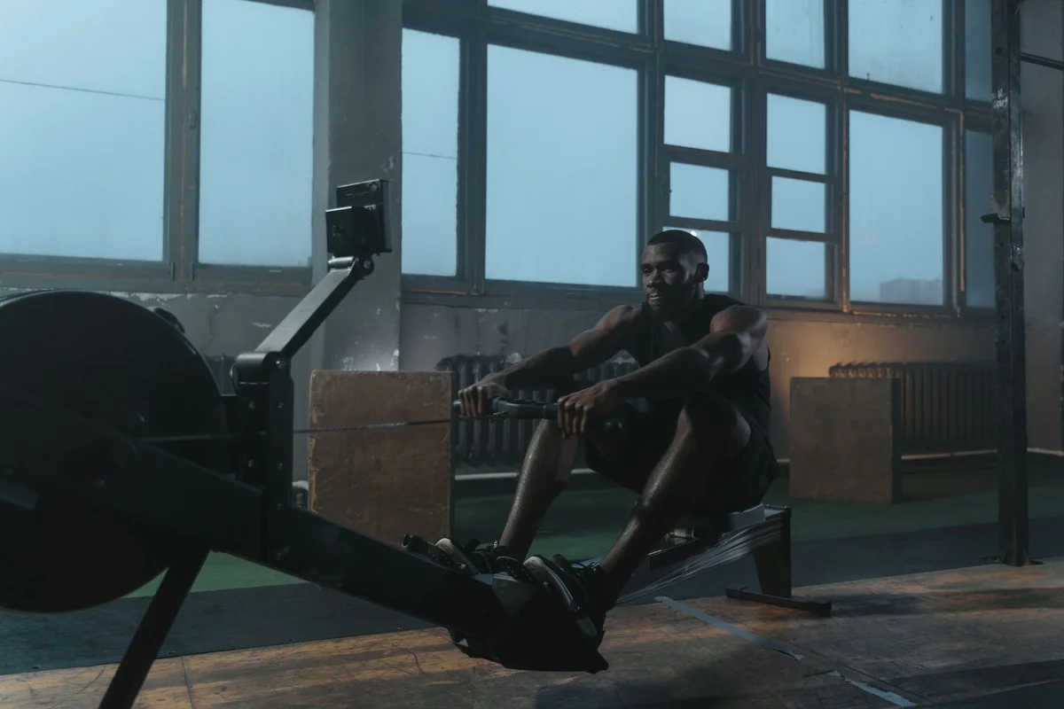 Man rowing on an indoor rowing machine in a gym with large windows
