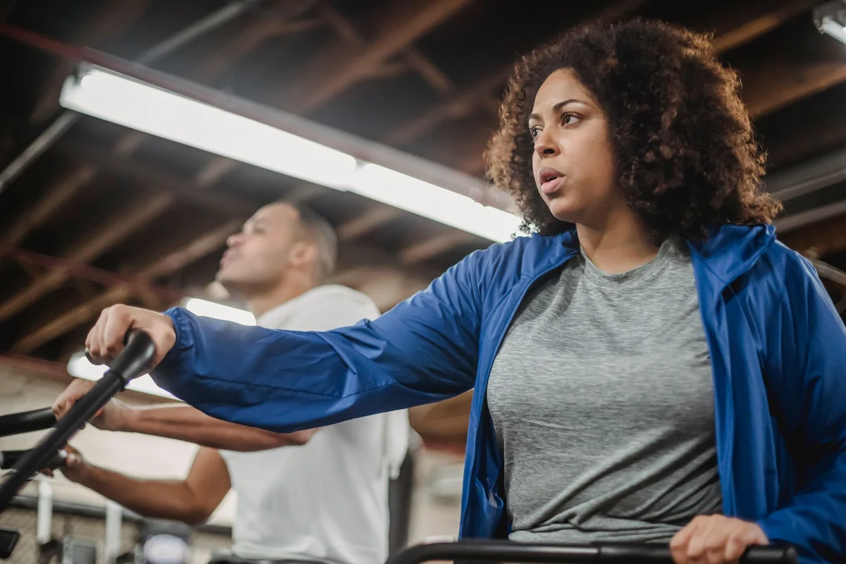 Woman and man working out intensely on stationary cardio machines in a gym setting