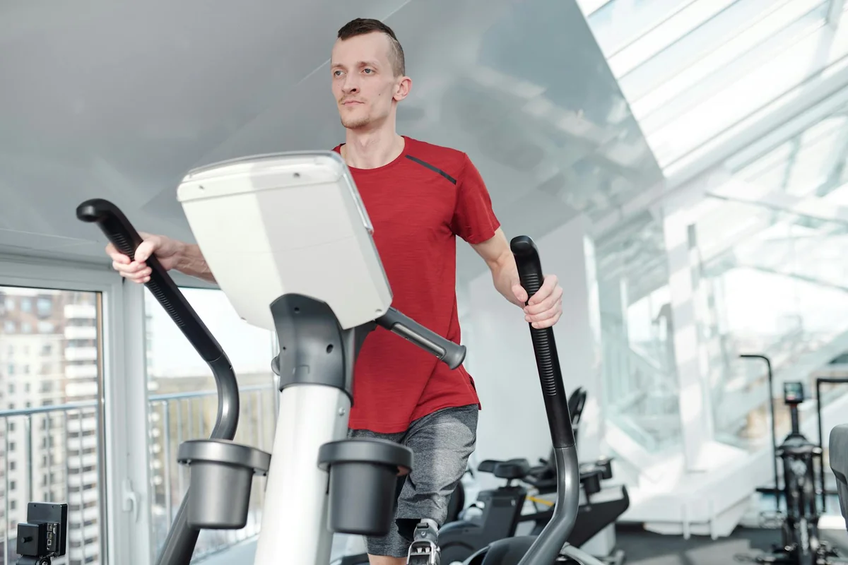 Man using an elliptical trainer in a bright modern gym with large windows and natural light