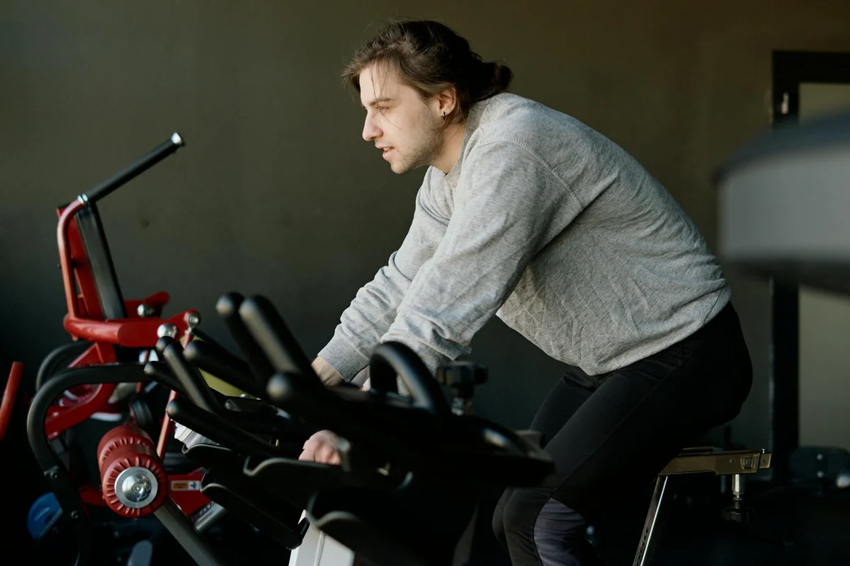 Man leaning forward on an upright stationary bike with a focused expression in a gym