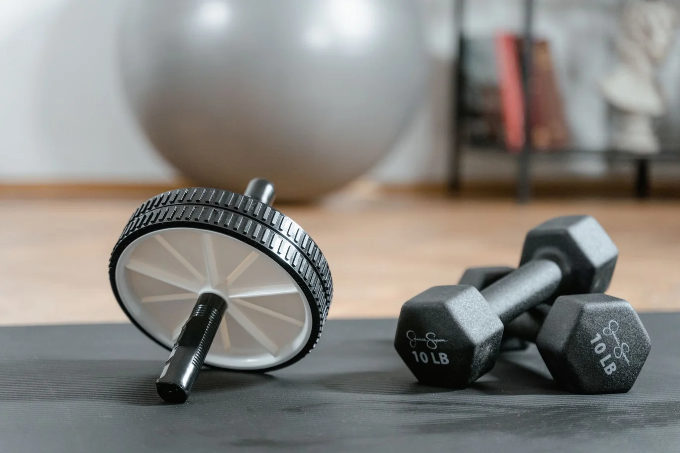 Ab wheel roller and pair of 10 lb dumbbells on a gray exercise mat in a home gym