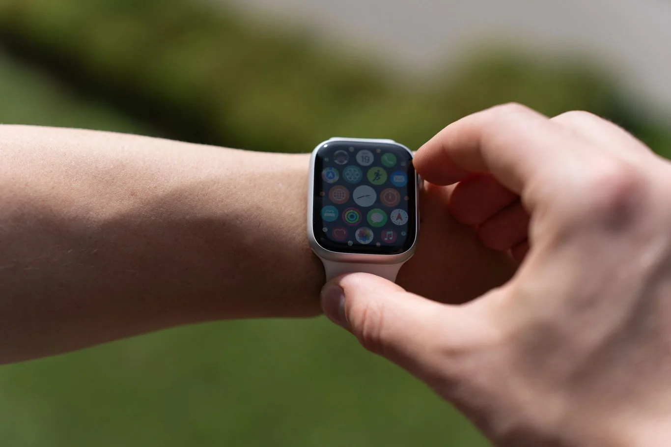 Smartwatch displaying colorful app icons on a wrist with blurred green outdoor background