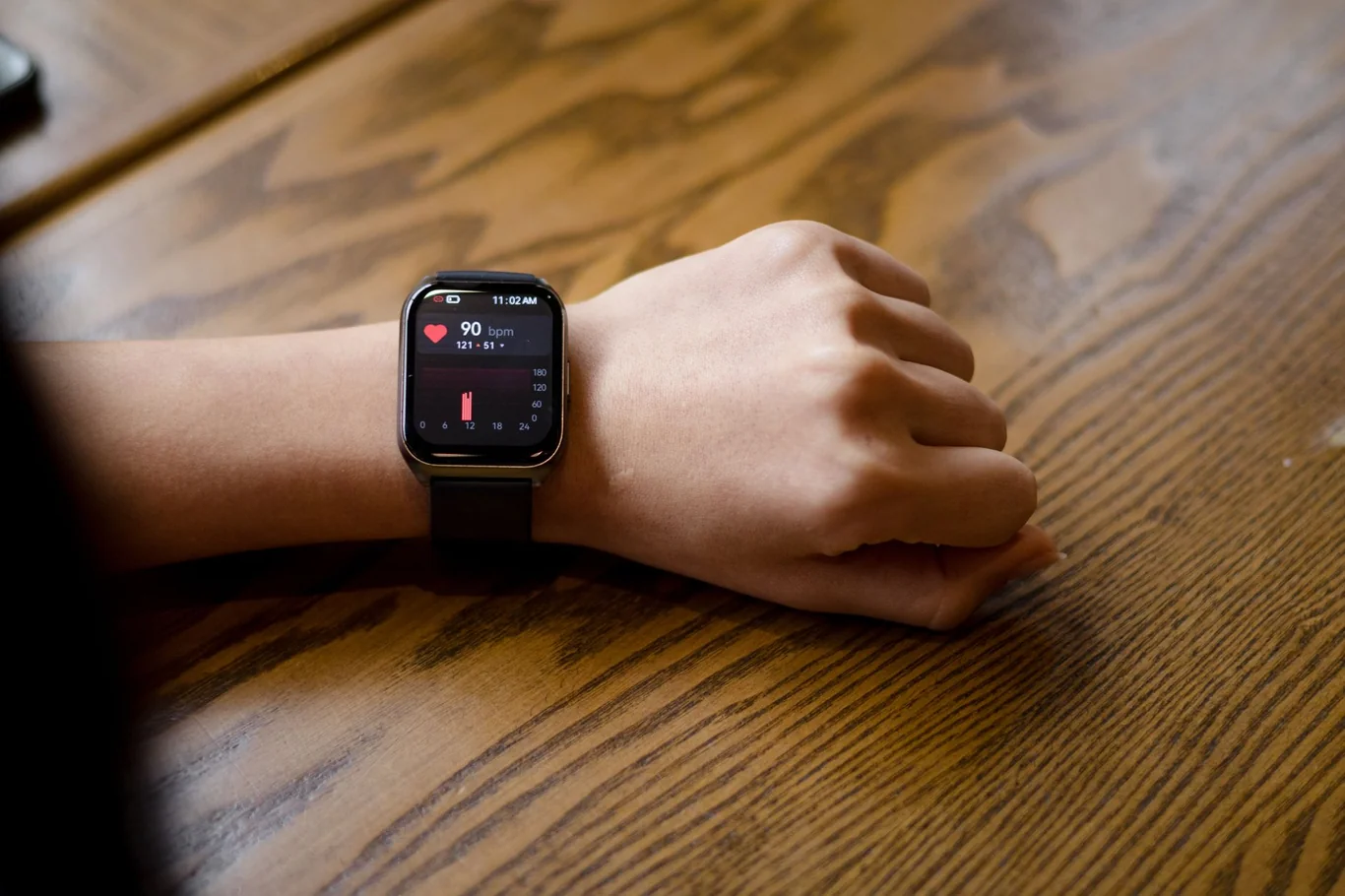 Black smartwatch on a wrist showing a heart rate reading on a wooden table