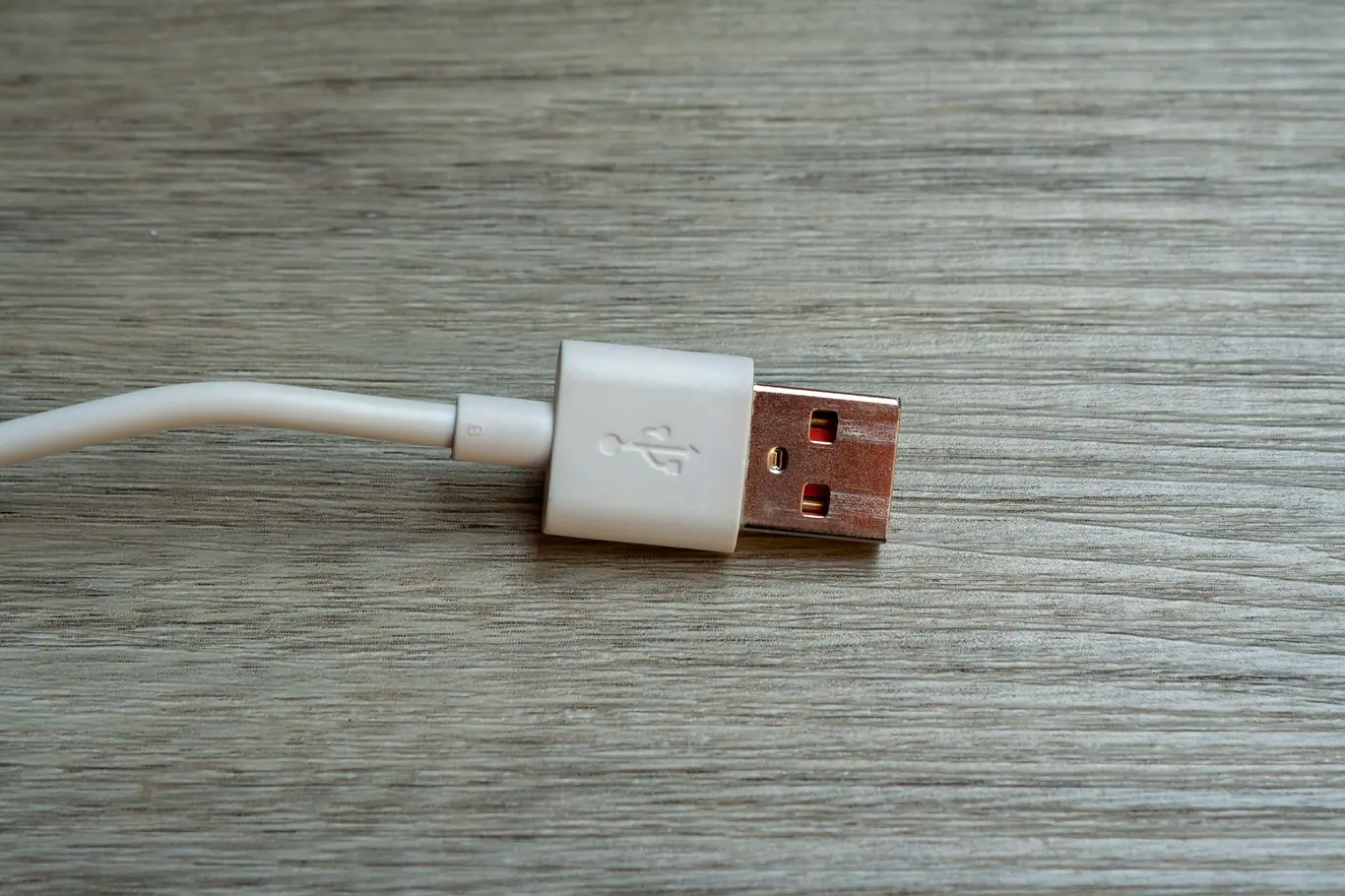White USB charging cable connector resting on a light wood grain table