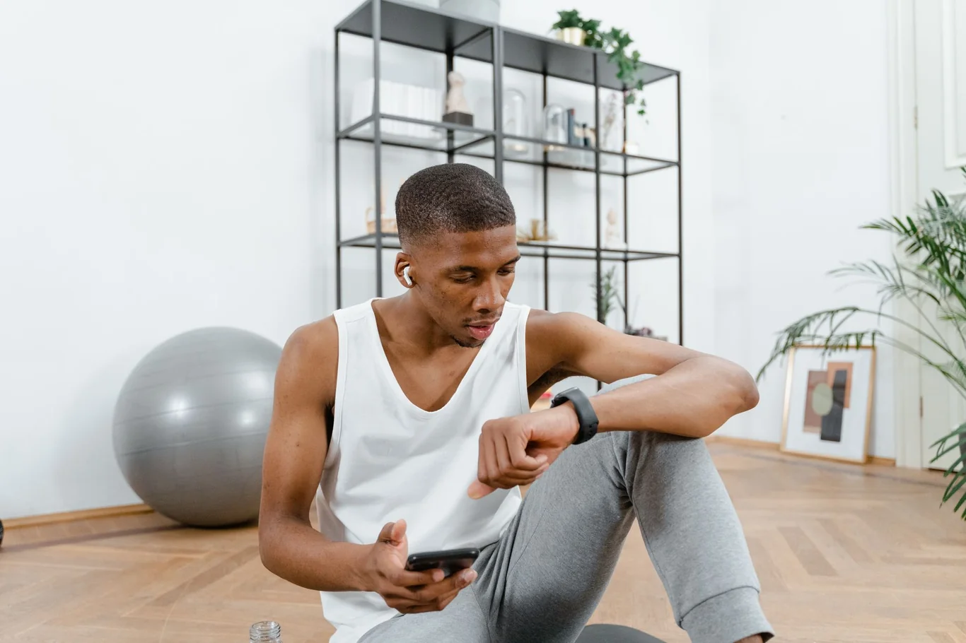 Man sitting on the floor at home checking his smartwatch while holding a phone