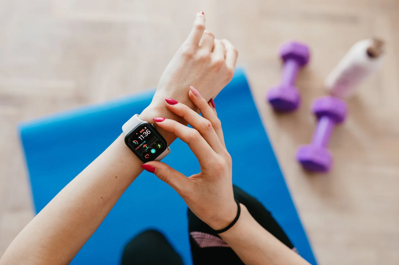Person checking a wrist fitness tracker beside a yoga mat and purple dumbbells