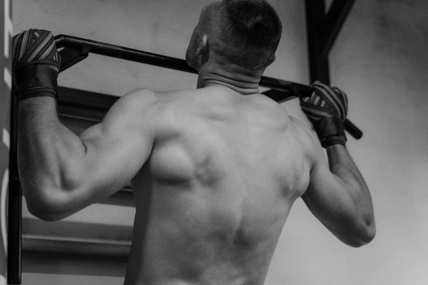 Back and shoulder muscles engaged mid pull-up, gripping the bar with wrist wraps