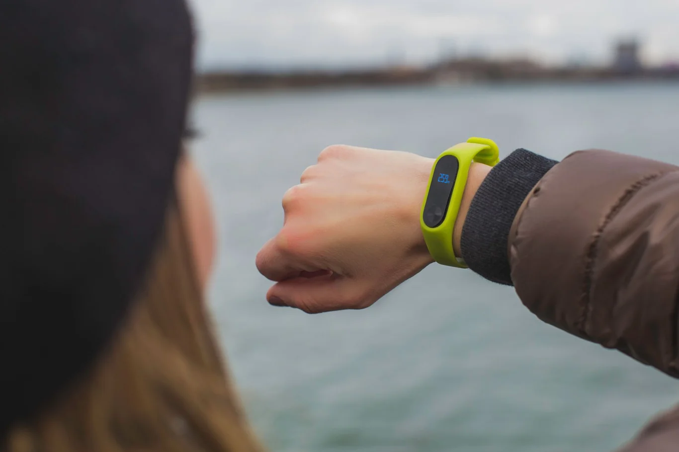 Green fitness tracker with digital display worn on a raised wrist outdoors