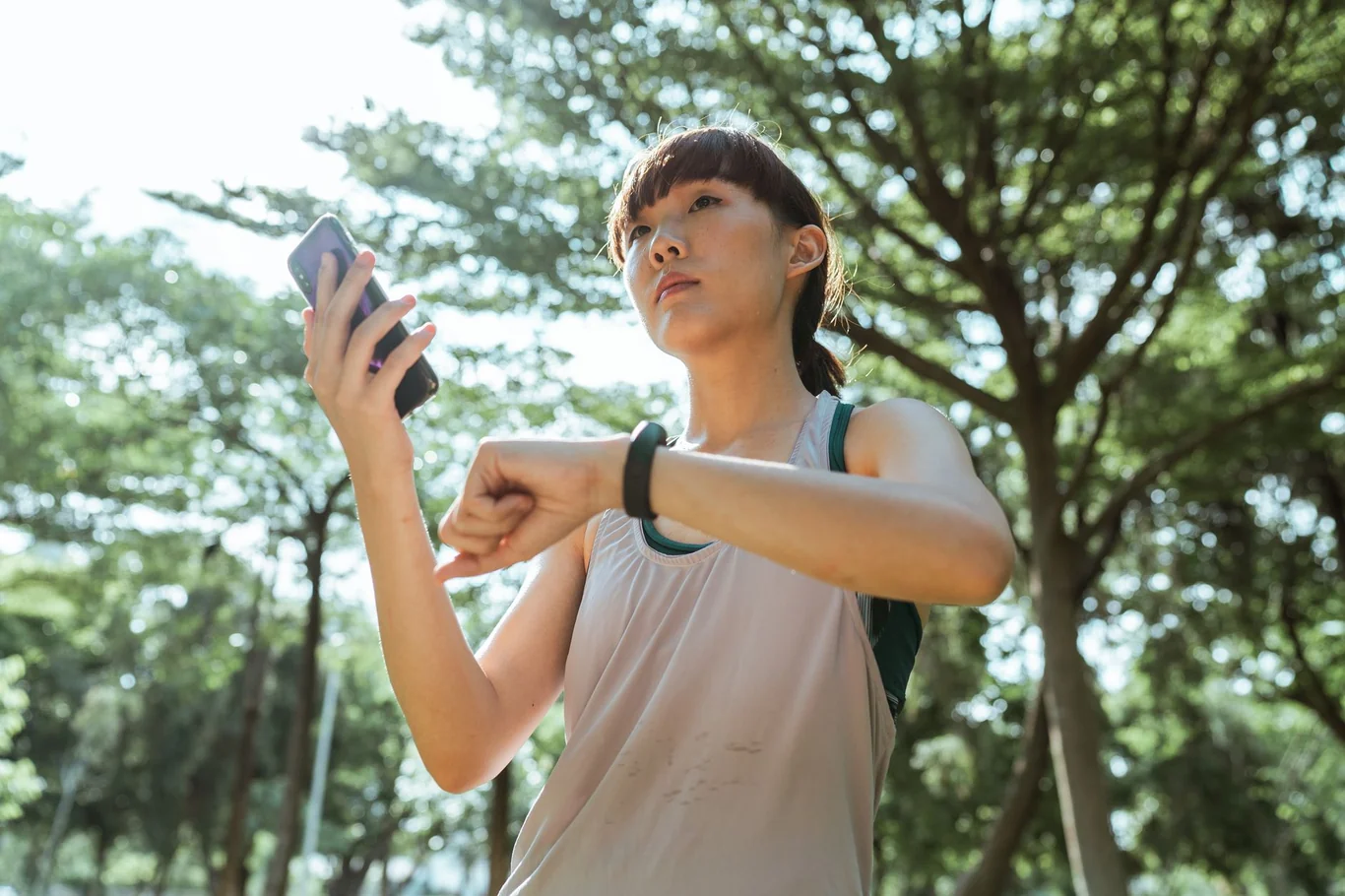 Woman in a park glancing at her wrist fitness tracker while holding a phone