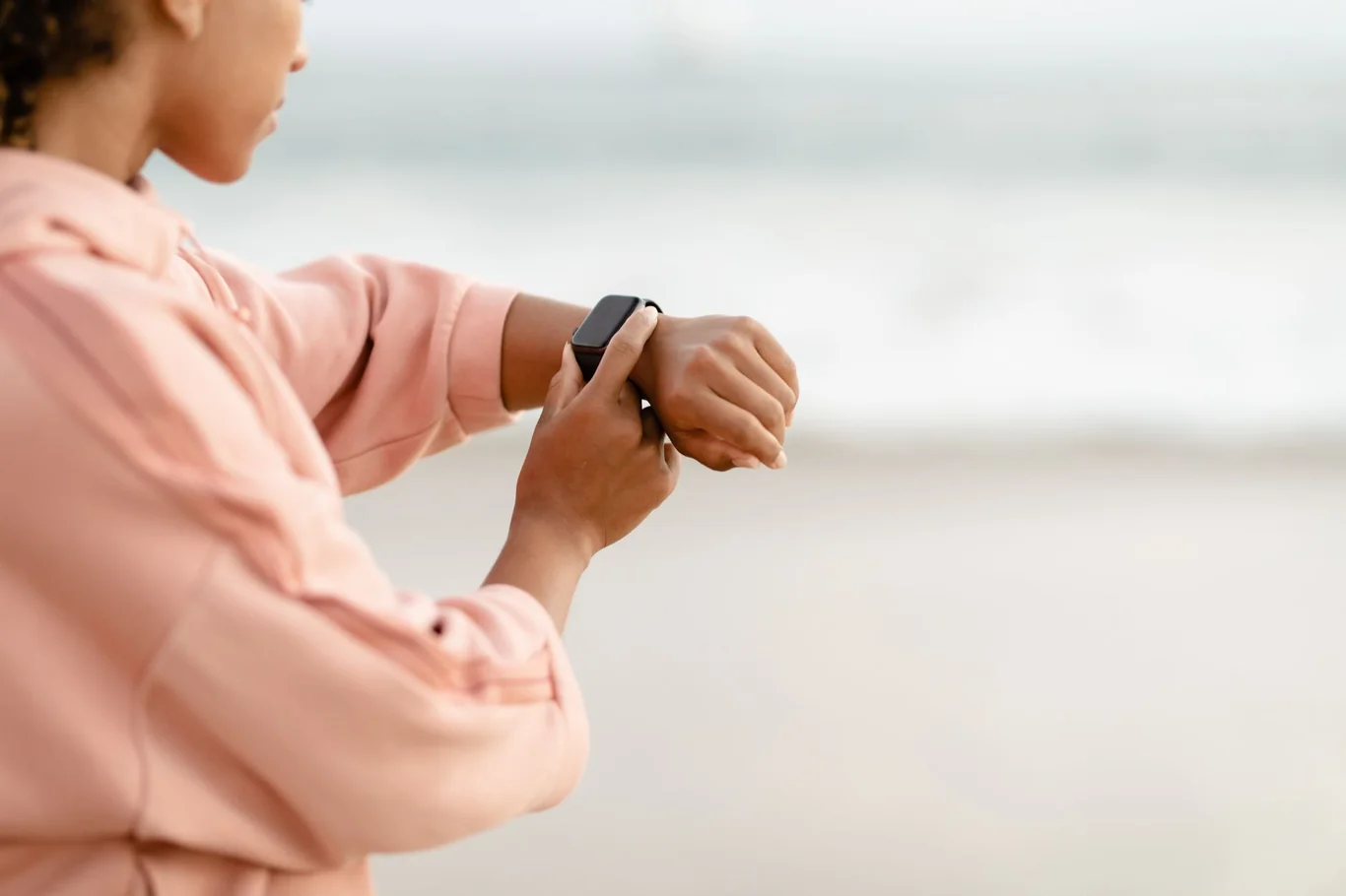Person in a pink hoodie checking a black fitness tracker on their wrist outdoors