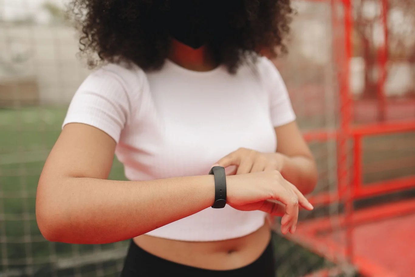 Woman in a white top checking her black fitness tracker band outdoors