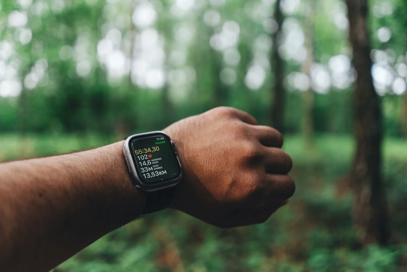 Smartwatch on a runner's wrist displaying stats on a wooded outdoor trail