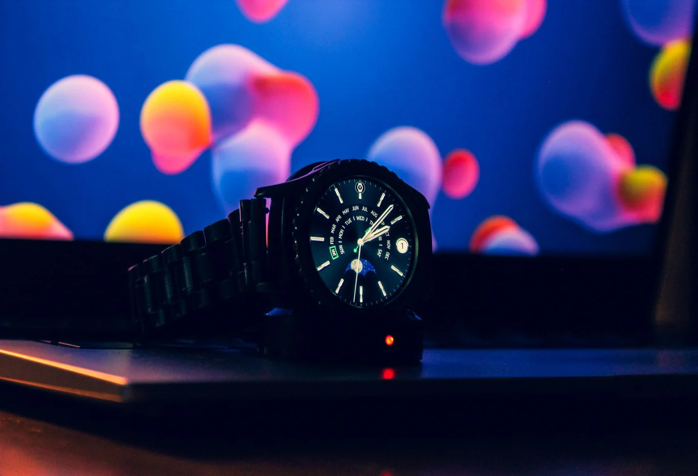 Black smartwatch with a metal band resting upright on a charging stand at night with blurred lights