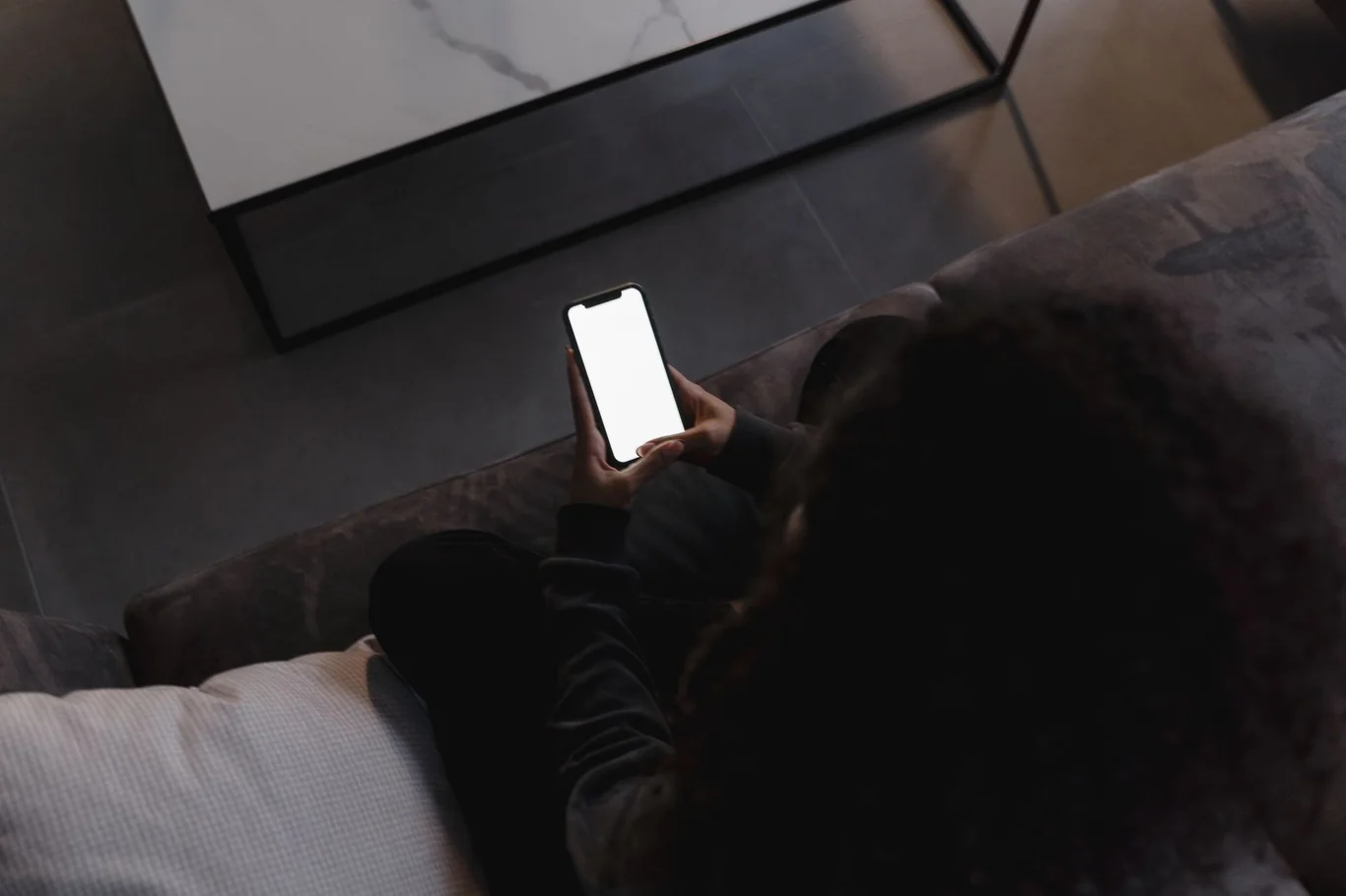 Overhead view of someone on a couch at home holding a blank smartphone screen