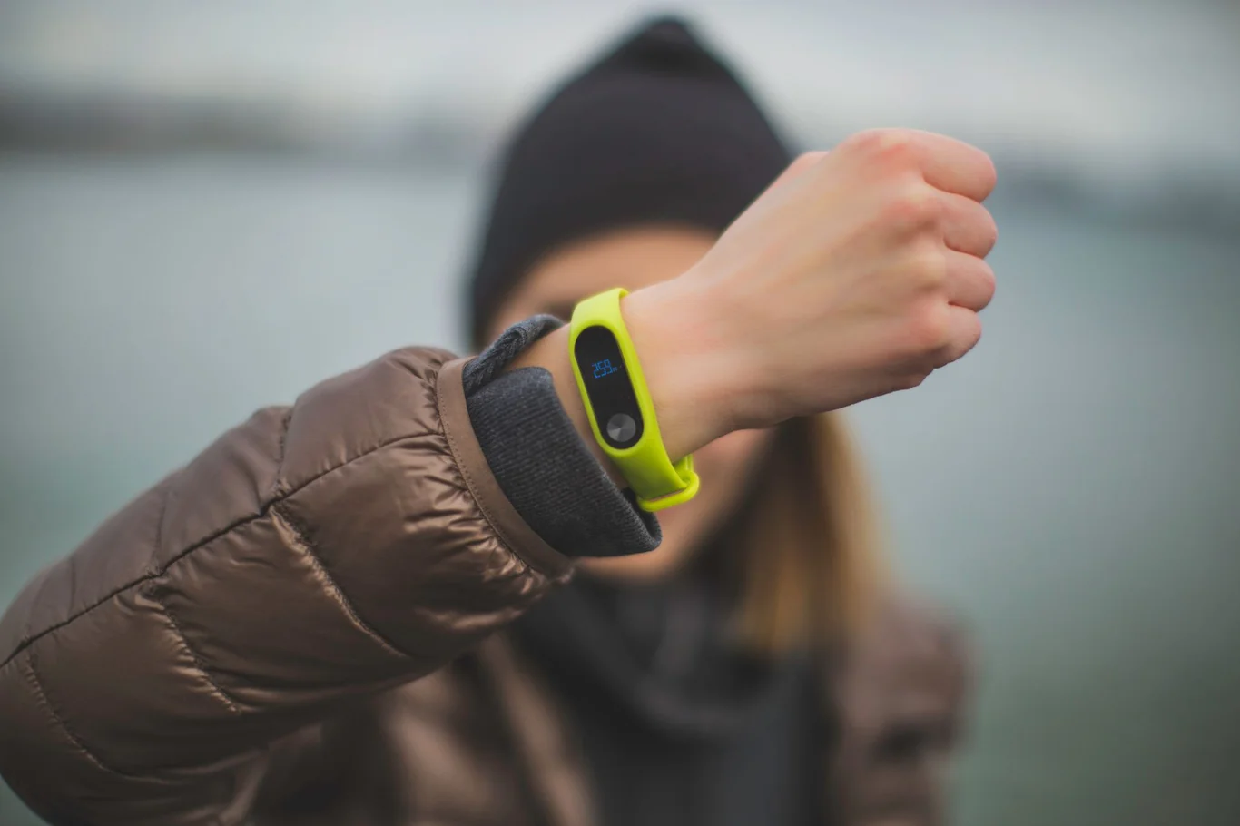 Person in a brown jacket wearing a bright green fitness tracker band outdoors
