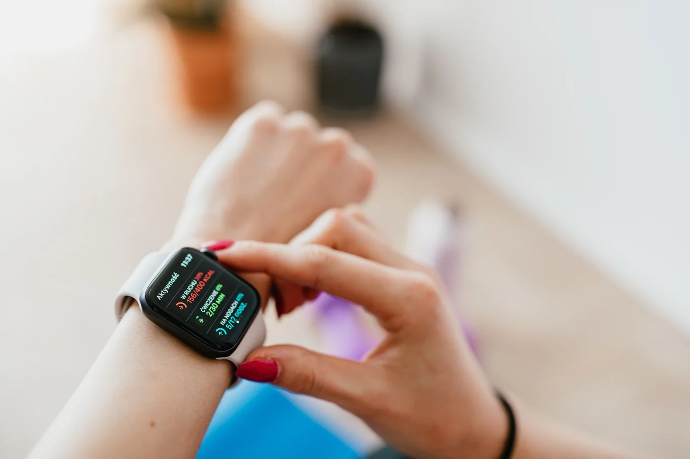 Hand with red nail polish checking a black smartwatch display in a home workout setting