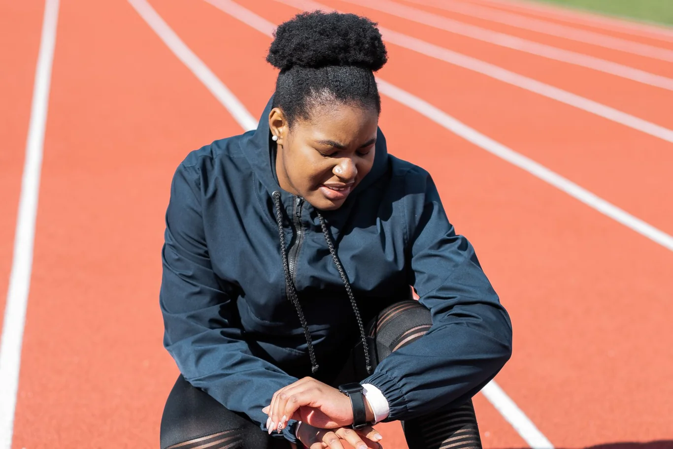 Runner crouched on a running track checking a watch on her wrist