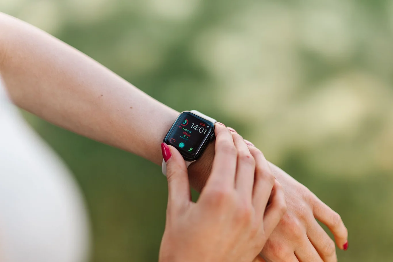 Close-up of a wrist wearing a black smartwatch showing the time and notification icons outdoors