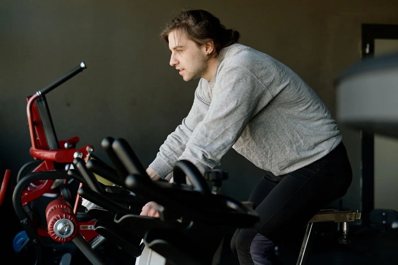 Man in a gray sweatshirt pedaling a stationary exercise bike with hands on the handlebars