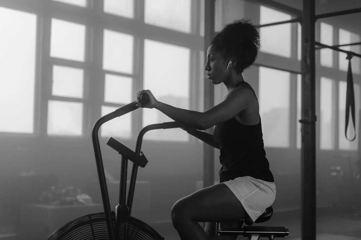 Woman pedaling an indoor fan bike with dual handlebars in a gym