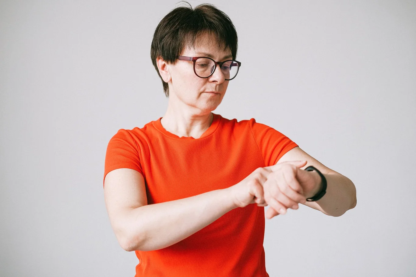 Woman with glasses checking her smartwatch on a plain background