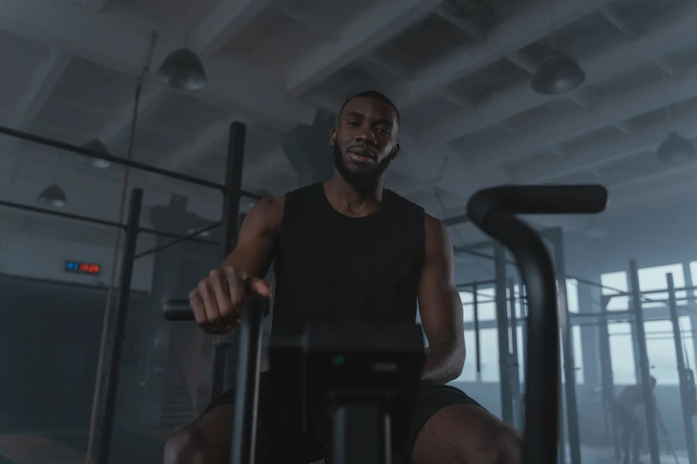 Man riding an exercise bike in a dim gym with overhead lighting