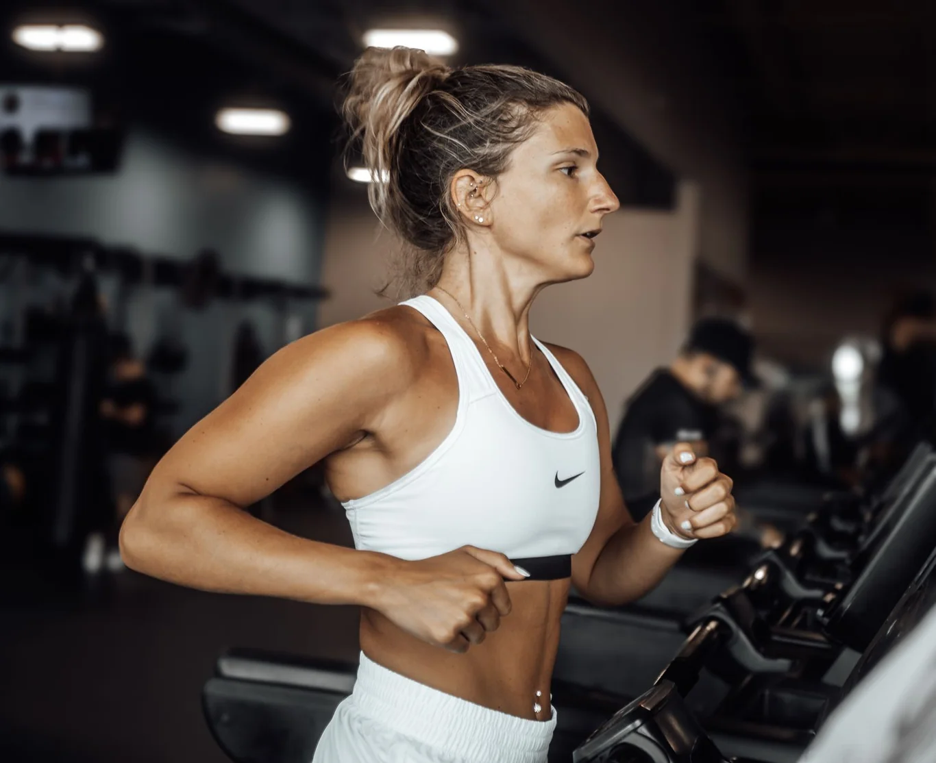 Woman running on a treadmill in a gym with arms bent and swinging at her sides